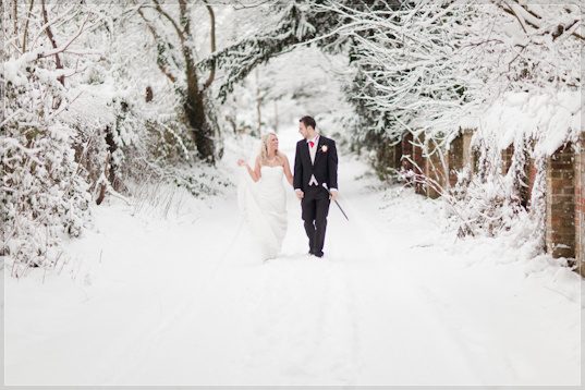 Nikki and Tom, bride and groom, walking in the snow on Shepherd's Lane, Hurley