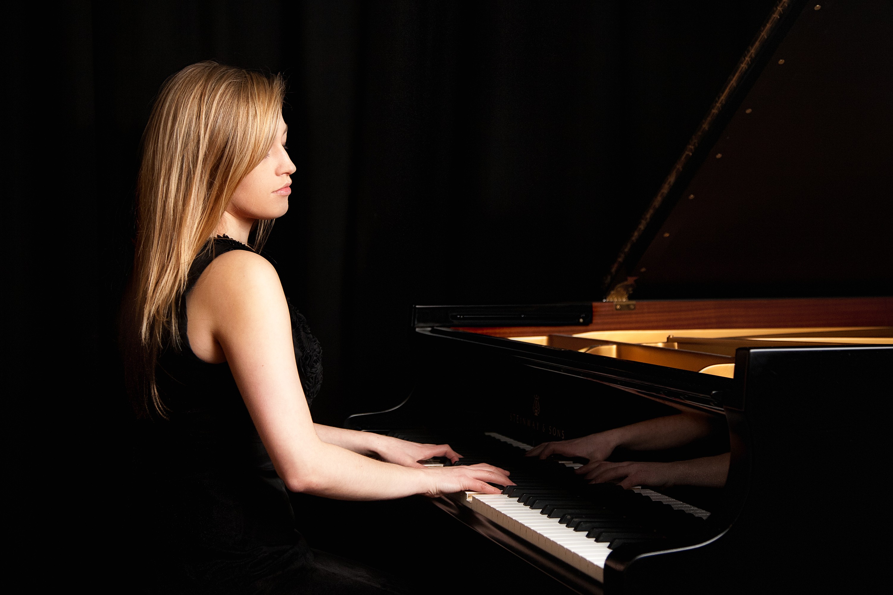 Ceri Owen, pianist, in a black dress playing a Steinway grand piano against a dark background, portrait by Mat Smith Photography, Magdalen College, Oxford