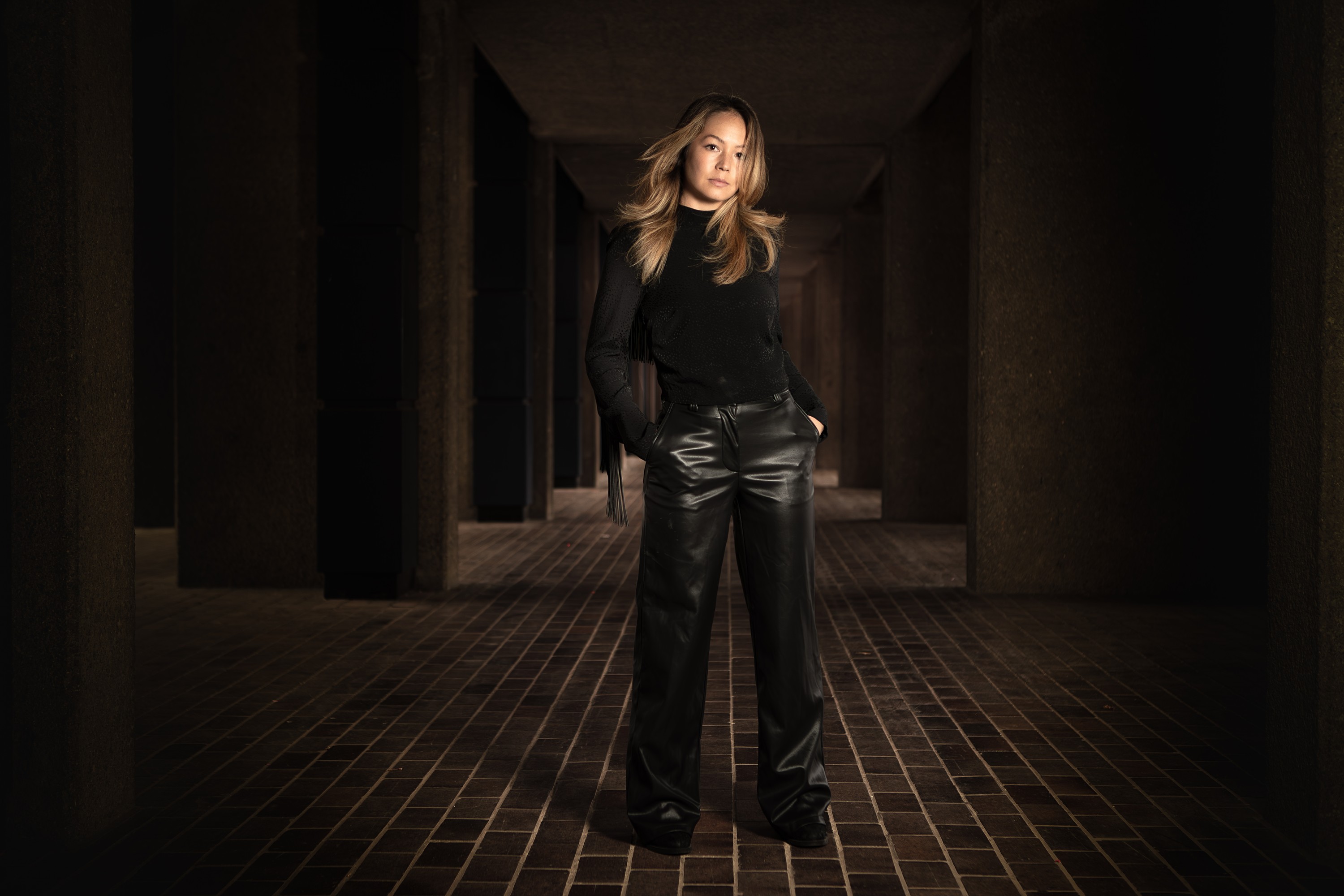 Emily Lim, composer, standing at the vanishing point of a long concrete walkway, portrait by Mat Smith Photography, the Barbican, London